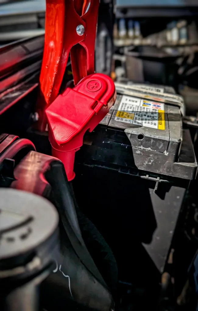 Car battery with red positive-terminal cover and cable attached — battery service at Rite-Price Auto Service Centre in Calgary, AB