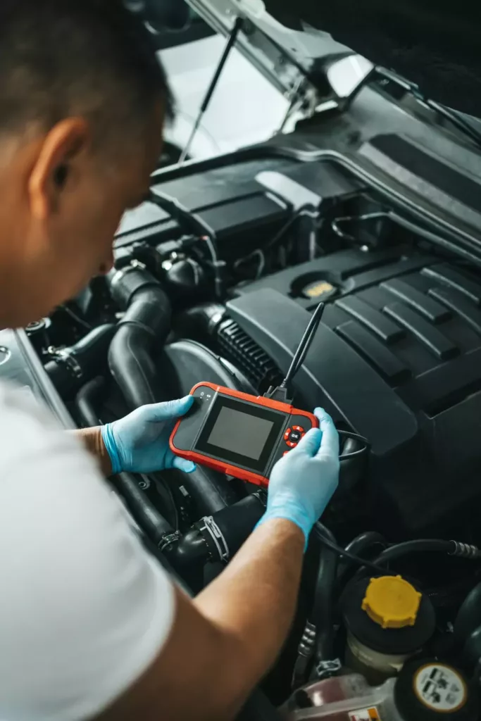 Mechanic using a handheld scan tool on an open engine bay for car electrical diagnosis at Rite-Price Auto Service Centre in Calgary, AB