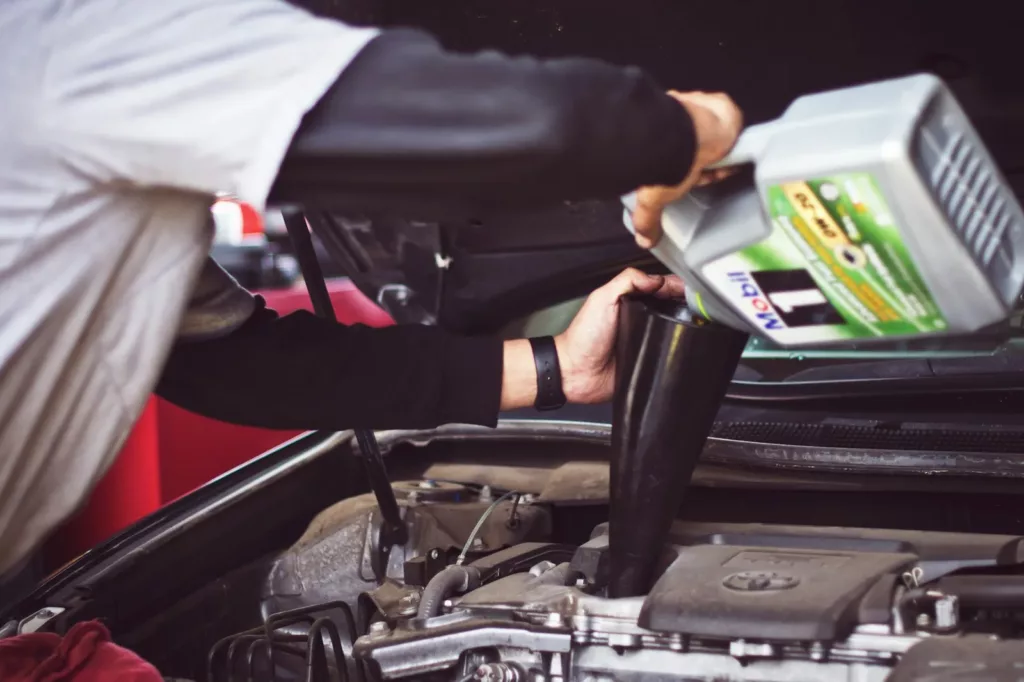 Mechanic pouring synthetic motor oil through a black funnel into the engine oil-fill port of a vehicle — synthetic oil change service at Rite-Price Auto Service Centre in Calgary, AB