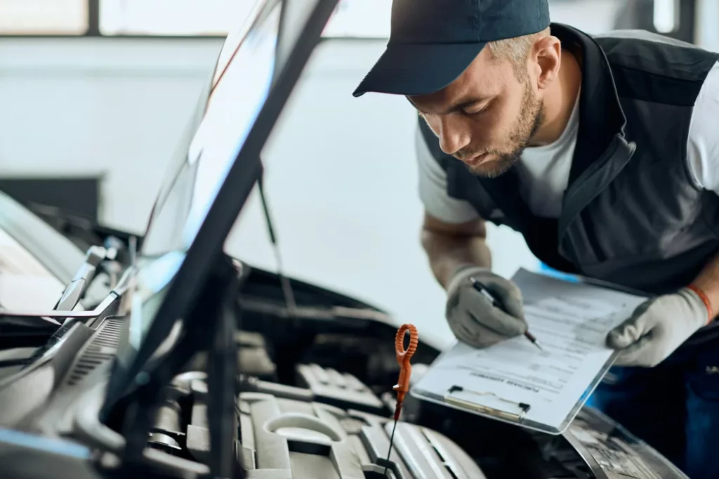 Mechanic filling out a pre-purchase vehicle inspection report on a clipboard while checking the engine bay at a Calgary auto shop — Rite-Price Auto Service Centre