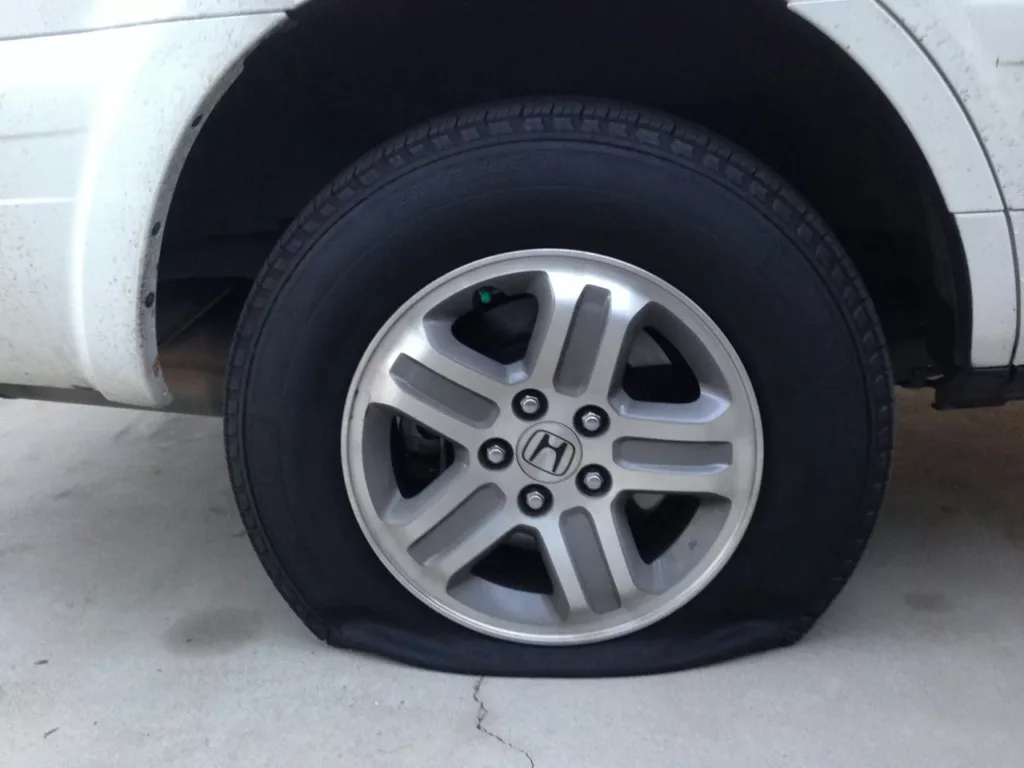 Underinflated tire on a Honda SUV showing a visible flat spot at the ground contact patch — the kind of low tire pressure that Calgary's temperature swings can cause, Rite-Price Auto Service Centre